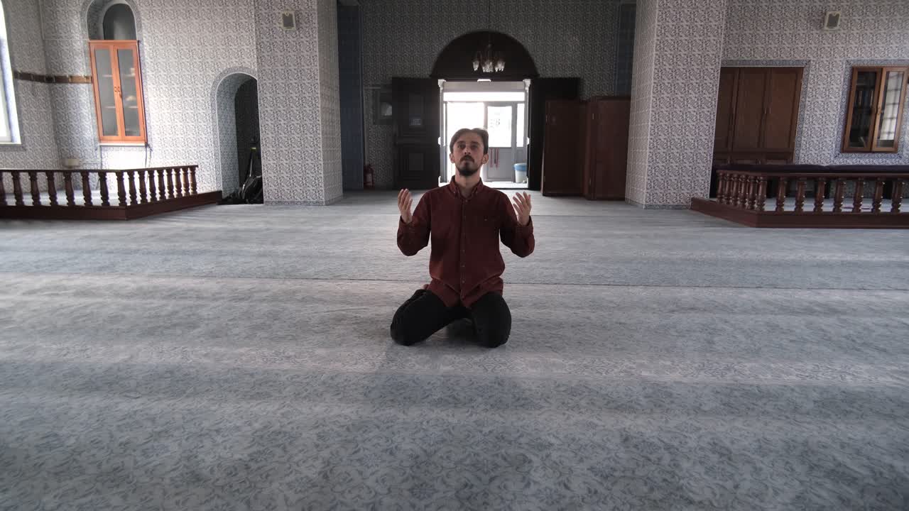 The young bearded man sitting inside a mosque praying to god with open hands, Muslims who go to historical and holy places pray