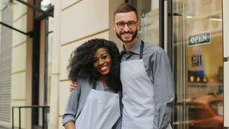 portrait of female and male waiters hugging and smiling at camera outside of a modern coffee shop