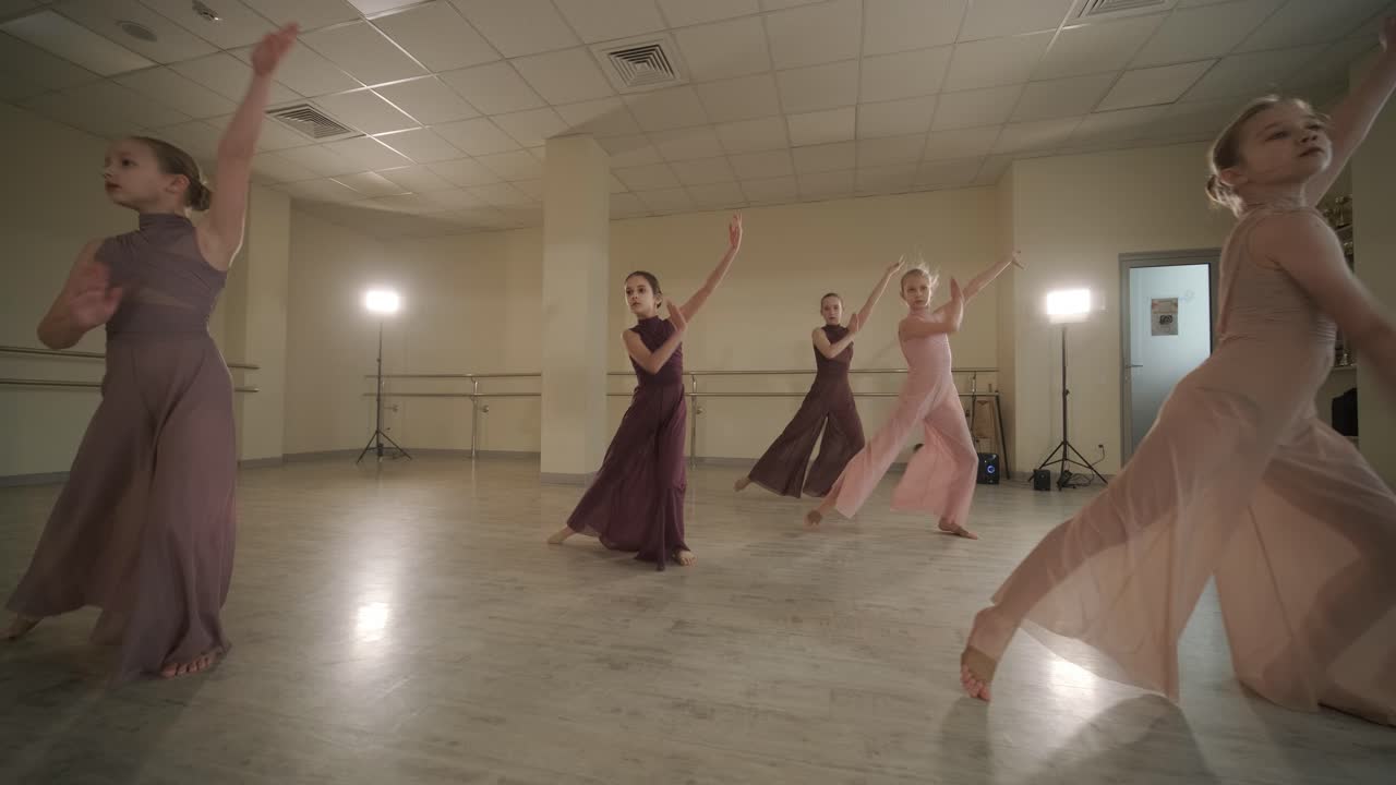 un grupo de jóvenes estudiantes de ballet con ropa de baile negra practicando posiciones en un amplio estudio de ballet con pisos de madera y barras montadas en la pared. expresiones enfocadas y movimientos sincronizados.