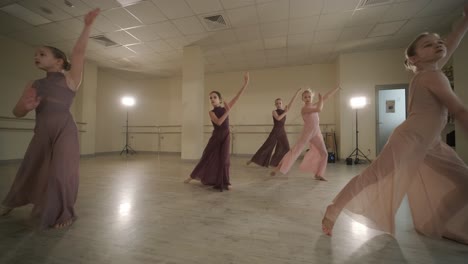 a group of young ballet students in black dancewear practicing positions in a spacious ballet studio with wooden flooring and wall-mounted barres. focused expressions and synchronized movements.