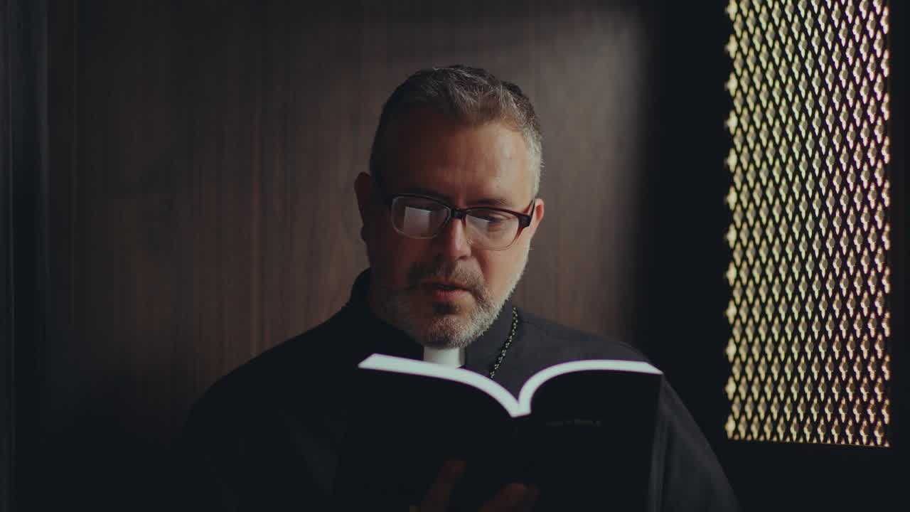 Catholic Priest Reading Bible and Praying in Confessional Booth