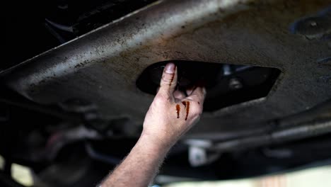 mechanic caucasian white man unscrewing and removing automobile oil filter from under car as oil drips and leaks all over, then pours out