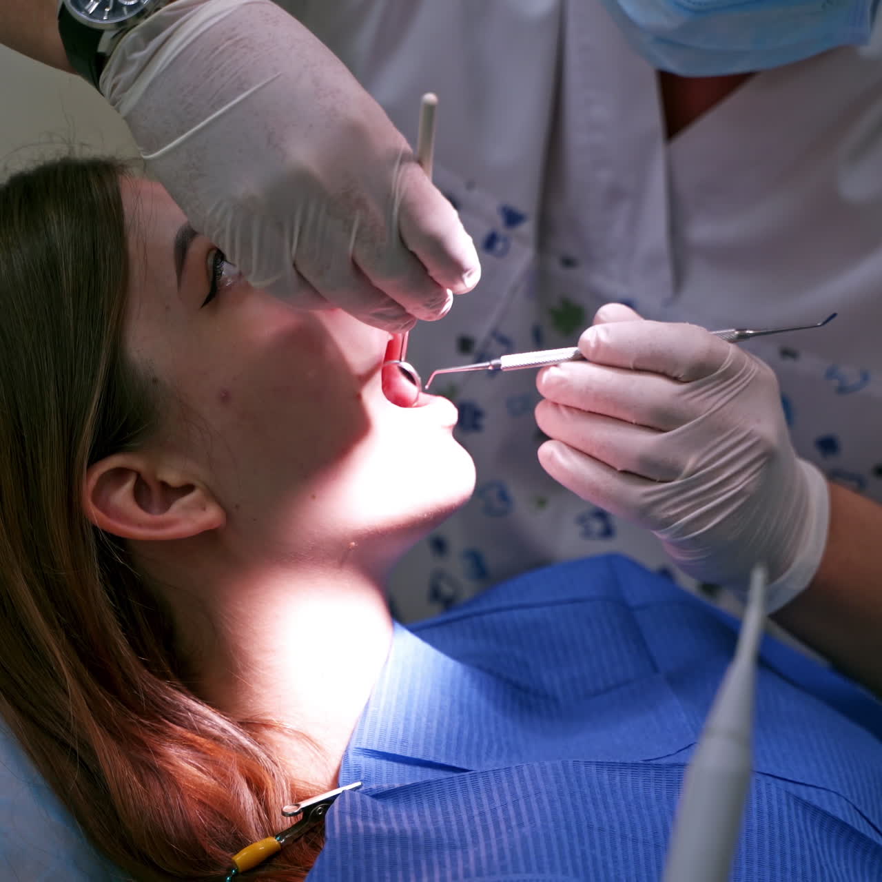 Doctor checks female's teeth. Close-up. Young woman with opened mouth at dentist's office. Stomatologist in sterile gloves treating patient.