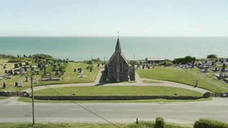 Vista-Aérea-De-La-Iglesia-De-San-Juan-Evangelista-Y-El-Cementerio-De-Ardamine-Con-El-Océano-Al-Fondo-En-Courttown,-Wexford,-Irlanda