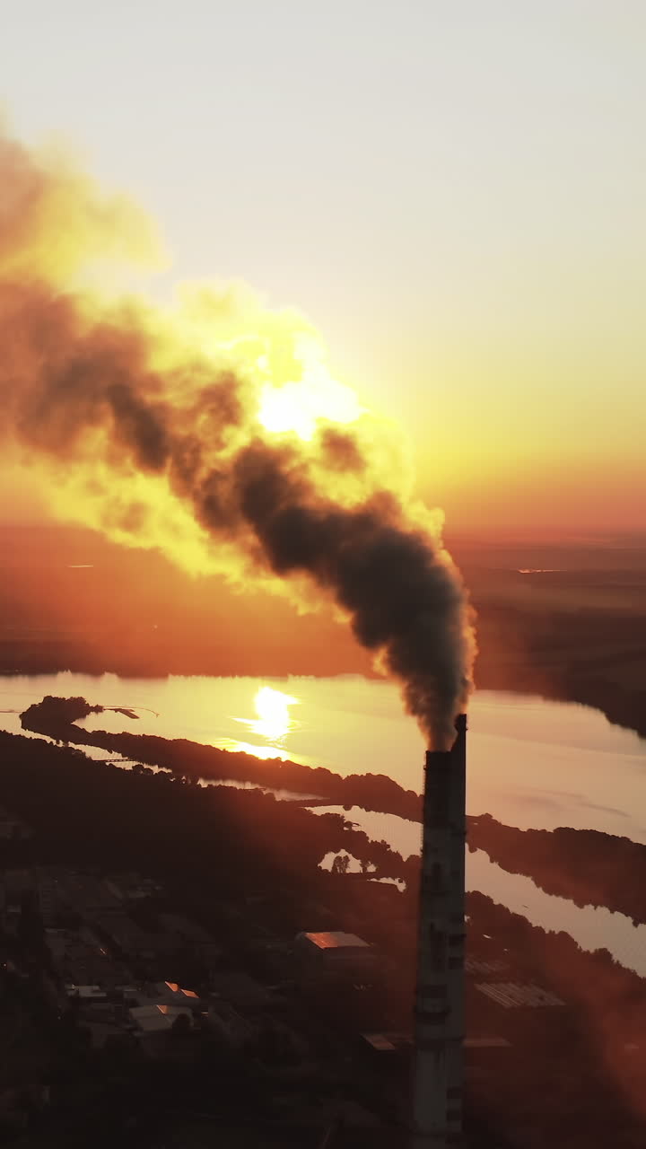 Pipes pollute atmosphere with smoke against the setting sun. Ecology pollution. Smoke stacks emit from industry on the background of lakes at sunset. Vertical video
