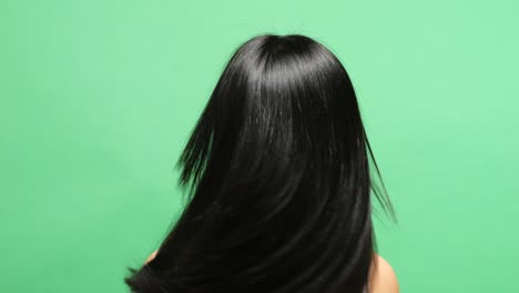 close up back view of a woman shaking her head showing her long and black straight healthy hair in the green screen background studio