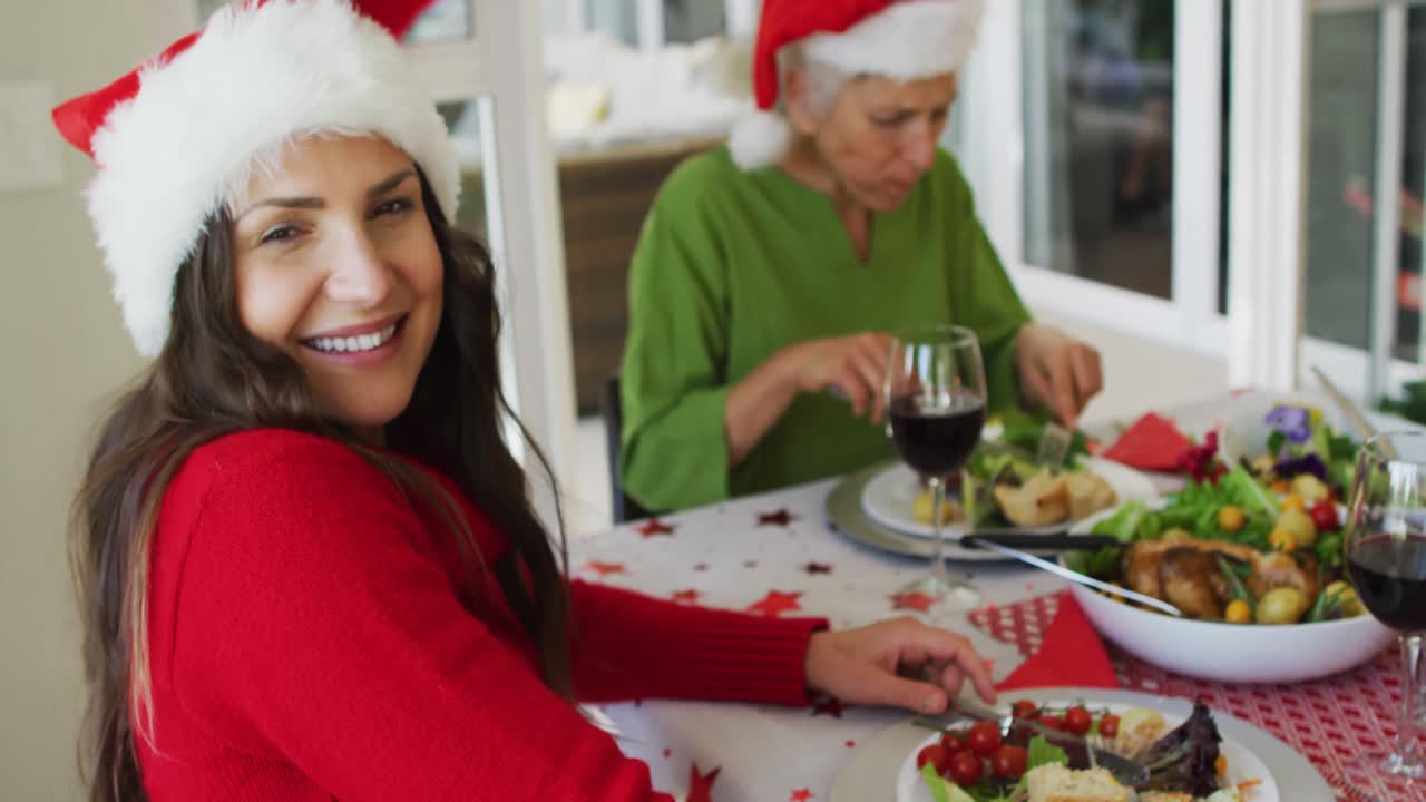 feliz mujer caucásica con sombrero de santa mirando a la cámara durante la comida de navidad