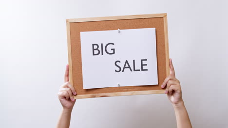 Woman's-hand-shows-the-paper-on-board-with-the-word-BIG-SALE-in-white-studio-background-with-copy-space