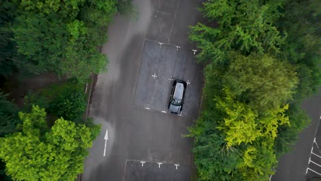 drone camera smoothly descends above a single parked car in a quiet, tree-lined parking lot at hope valley, england, under soft natural daylight