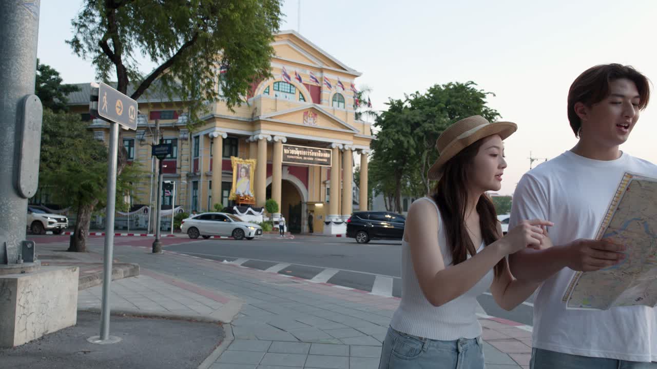 Young couple consults paper map on busy city street with temple architecture and passing traffic