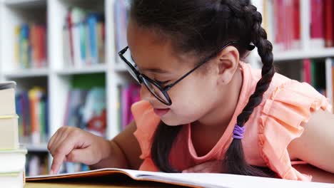 Schoolgirl-reading-book-in-library-at-school