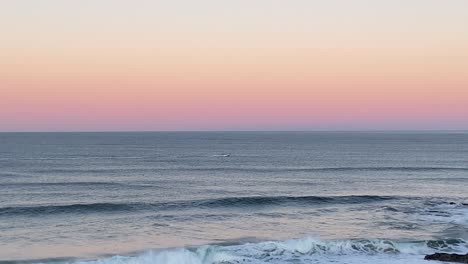 Magic-pink-sea-sunset-with-boat-sailing-near-of-rocks-in-Guincho