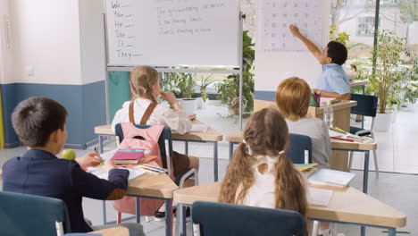 student sitting at the teacher's desk teaches the letters to his classmates in english classroomes