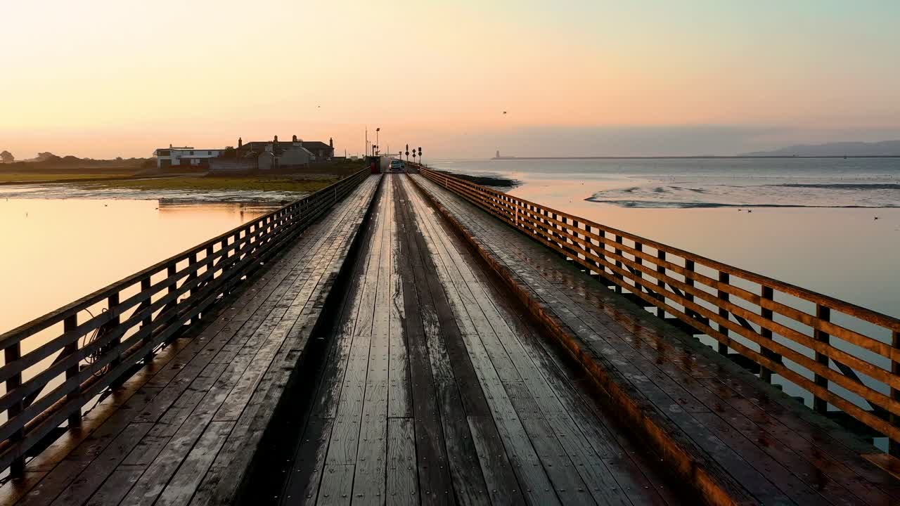 tiro de un dron de un viejo puente de madera en inglaterra durante las horas de la puesta del sol con casas al otro lado del puente