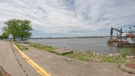 pov driving slowly along banks of mississippi river, past a small dredge barge with excavator bucket