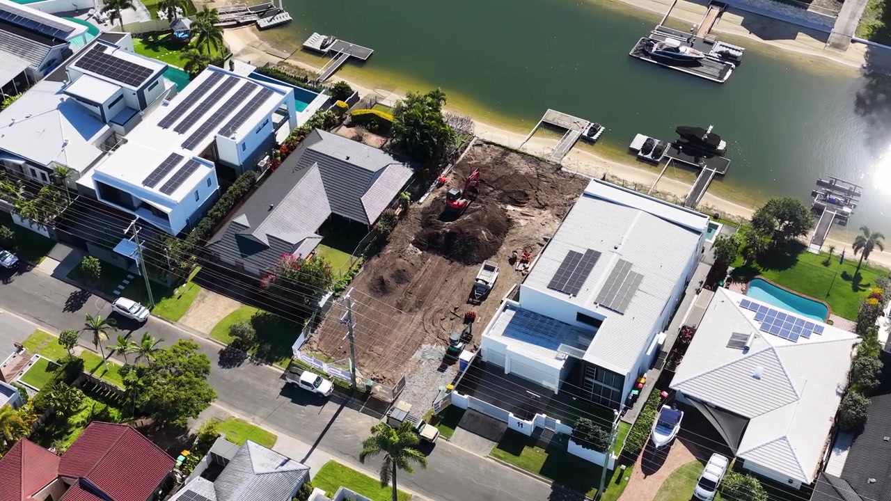 High-angle drone shot over luxury canal homes and an active residential construction site.