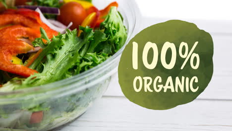 animation of 100 percent organix text in green over fresh organic vegetable salad in bowl on wood