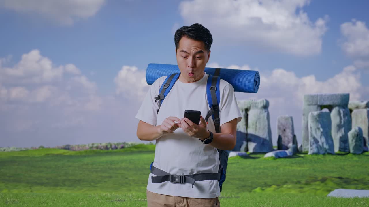 Asian Male Hiker With Mountaineering Backpack Looking At The Smartphone And Saying Wow While Traveling In Stonehenge