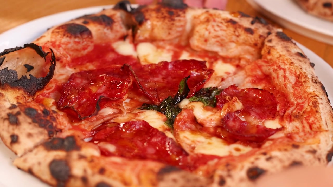 Mano che tira una fetta di pizza al salame appena sfornata