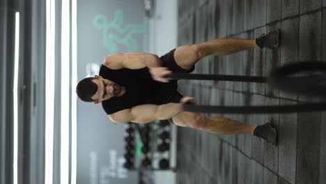 hombre musculoso atractivo que trabaja en el gimnasio usando cuerdas de batalla con alta intensidad