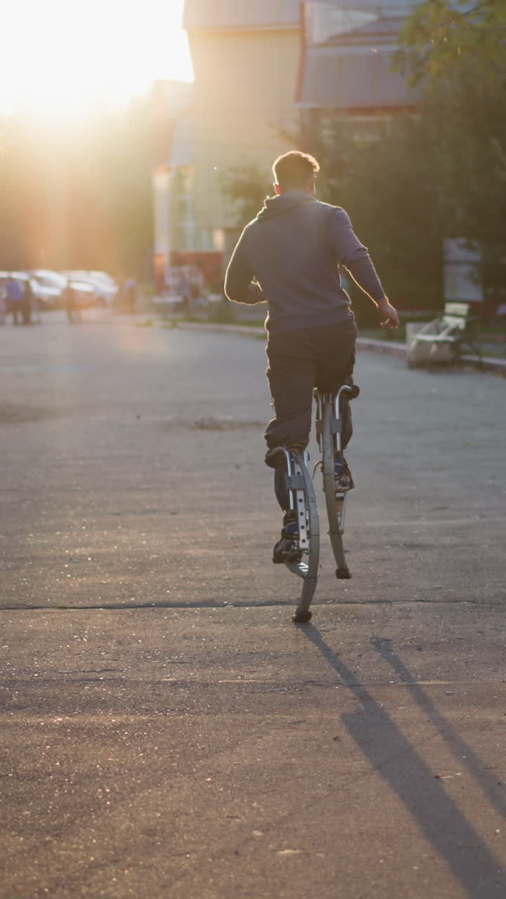 주거 지역의 포장 된 도로를 따라 발바닥에 달리는 젊은 남성, 늦은 오후 또는 이른 저녁에 뒤에서 잡혔습니다. 어두운 회색 파란색 스웨트 셔츠와 어두운 바지를 입고, 부드러운 빛으로