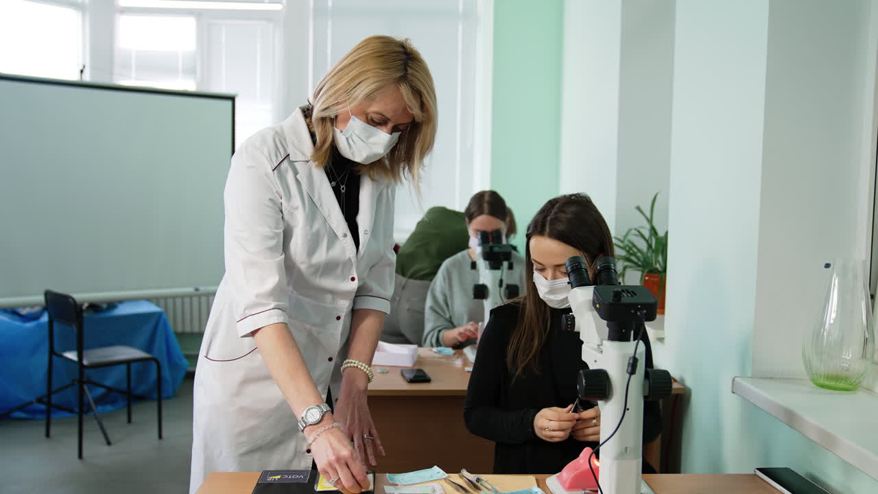 Interaction of a teacher and a student at practical lessons. Professor in mask showing the materials for work to a future medic.