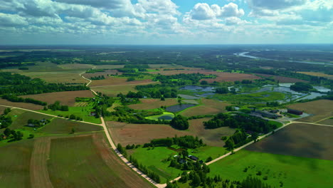 Aerial-of-rural-landscape-on-sunny,-cloudy-day,-winding-roads-and-lake