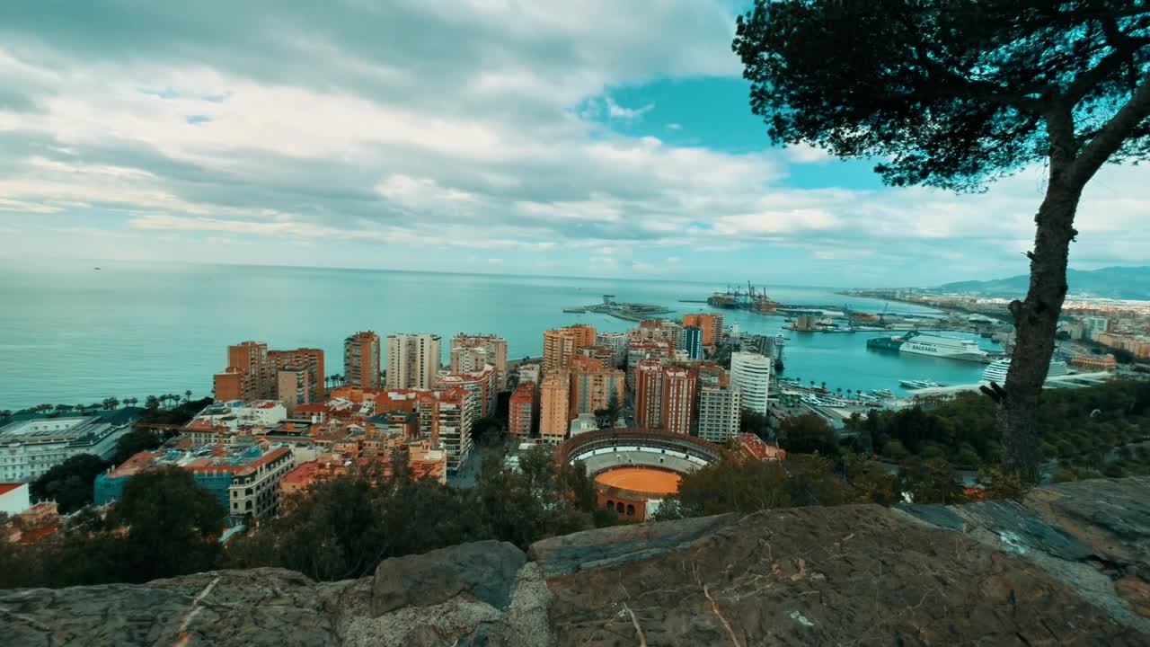 Aerial drone panorama of Malaga with terracotta rooftops, historic bullring, harbor, and calm Mediterranean Sea framed by coastal cliffs and soft daylight creating scenic urban view
