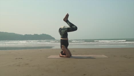 slow controlled headstand teaching vinyasa yoga class on beach to students