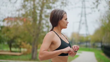 back view of sporty woman stretching waist outdoors in park, focused on improving flexibility, surrounded by trees in blurred background, enjoying healthy outdoor exercise routine