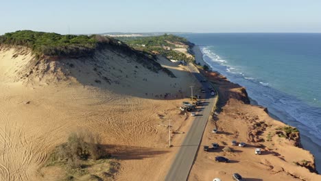 Dolly-in-aerial-drone-shot-of-the-popular-tourist-destination-the-Cacimbinhas-Sand-Dunes-with-people-sand-boarding-near-Pipa,-Brazil-in-Rio-Grande-do-Norte-on-a-warm-sunny-summer-day