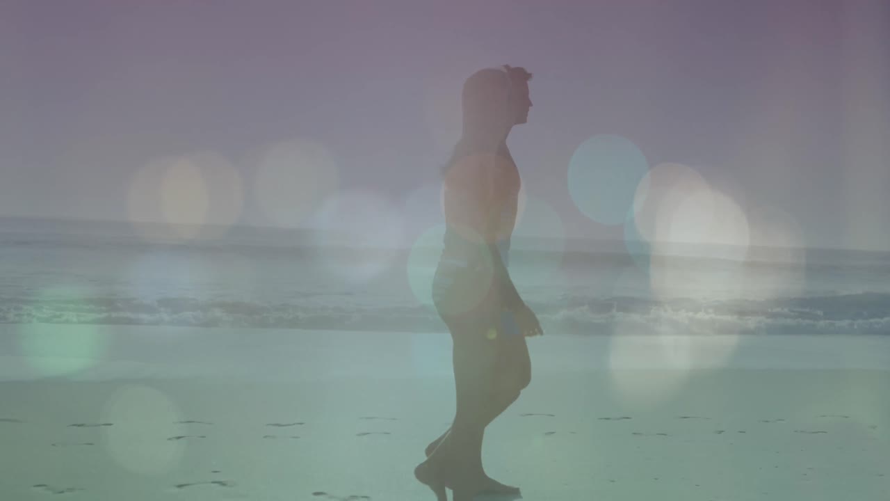 Animazione di bagliori di lente su una coppia caucasica in silhouette che cammina in spiaggia durante una giornata di sole.