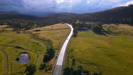 Toma-Aérea-Hacia-Adelante-De-La-Hermosa-Zona-De-Crackenback-Con-Una-Carretera-Alpina-En-Frente-Y-Montañas-Al-Fondo-En-Un-Día-Soleado-En-Nueva-Gales-Del-Sur,-Australia