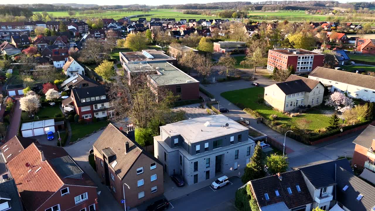 Modern Apartment houses and residential during Sunset time in small german city. Rooftop of school during spring day. Aerial top down flyover shot. Rural farm fields in background.