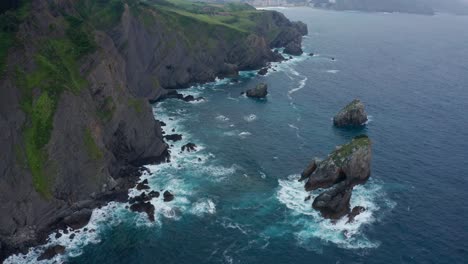 Mossy-cliffs-near-foamy-ocean-in-daylight