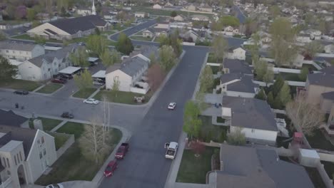 Vista-De-Drones-De-La-Conducción-De-Automóviles-En-Un-Barrio-Suburbano-Por-La-Noche-Tirando-Hacia-Atrás-Revelando-Montañas