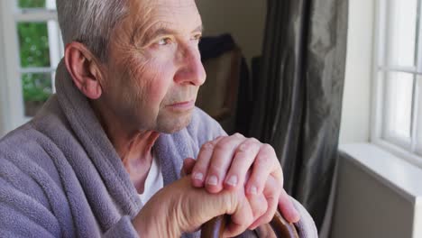 sad senior caucasian man wearing bathrobe sitting by window