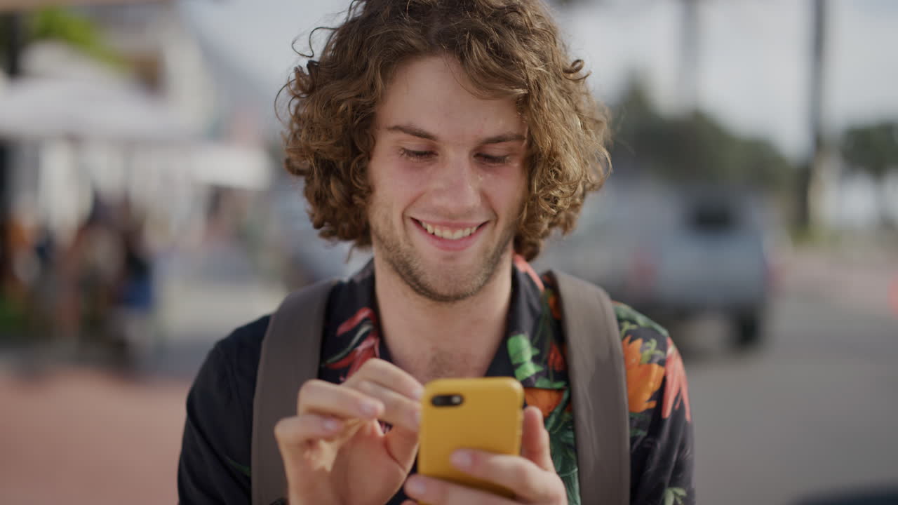 portrait of young caucasian man using smartphone browsing online texting sharing messages on summer vacation enjoying mobile communication in sunny urban beachfront