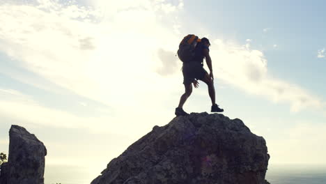 man reaching the top of a mountain against sunset