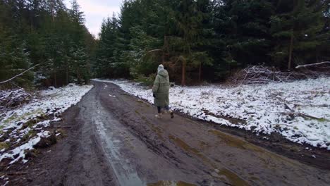 a girl dressed in a warm winter jacket is walking along a muddy path in the forest