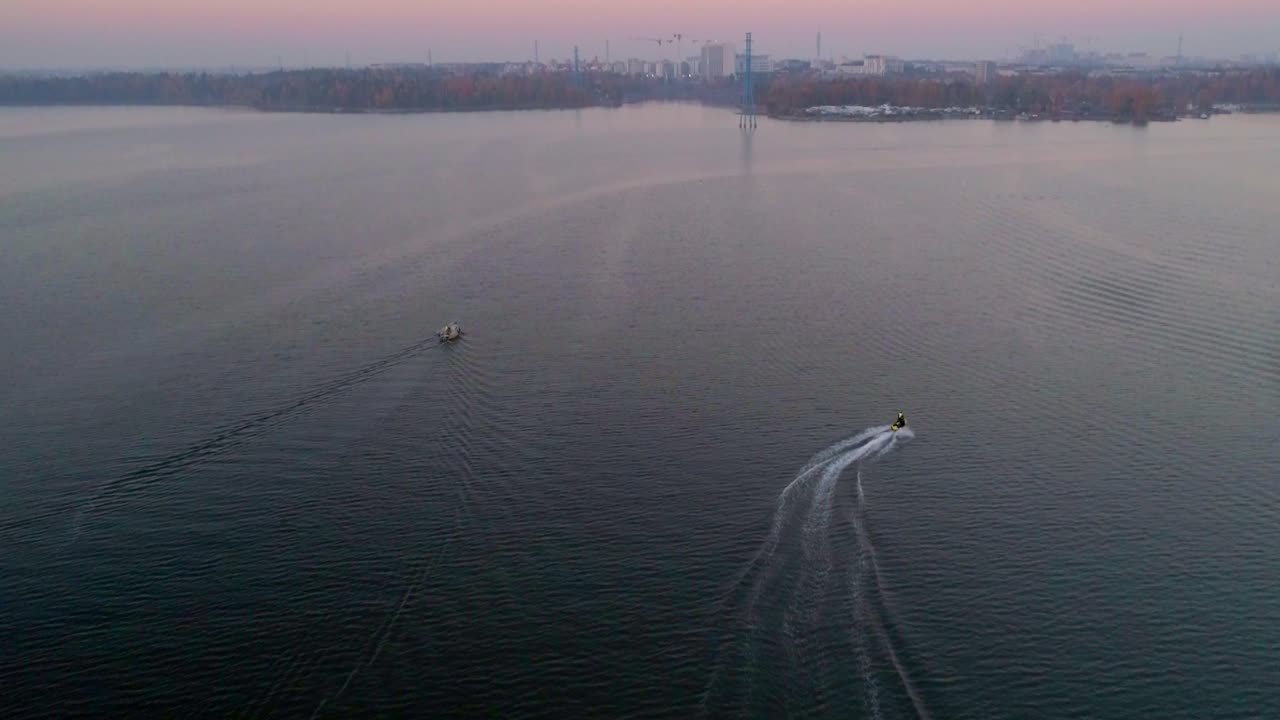 Aerial,tilt up, drone shot, following a water scooter jet, driving over the sea, between lauttasaari and Hietaniemi, on seurasaarenselka, on a sunny and misty, autumn evening, in Helsinki, Finland