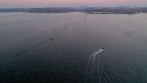 aerial,tilt up, drone shot, following a water scooter jet, driving over the sea, between lauttasaari and hietaniemi, on seurasaarenselka, on a sunny and misty, autumn evening, in helsinki, finland
