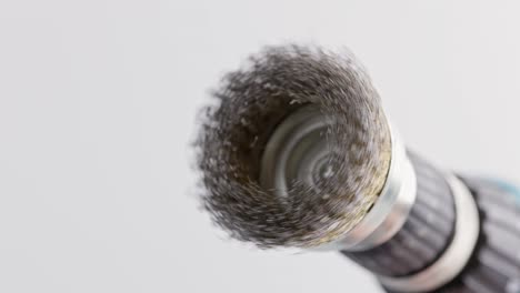 hand drill with round steel brush spinning on white background