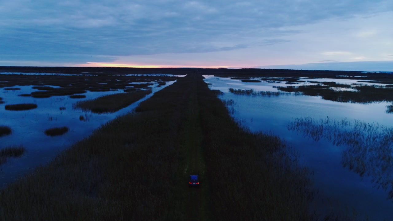 Aerial cinematic of vehicle moving forward through wetlands at dusk twilight
