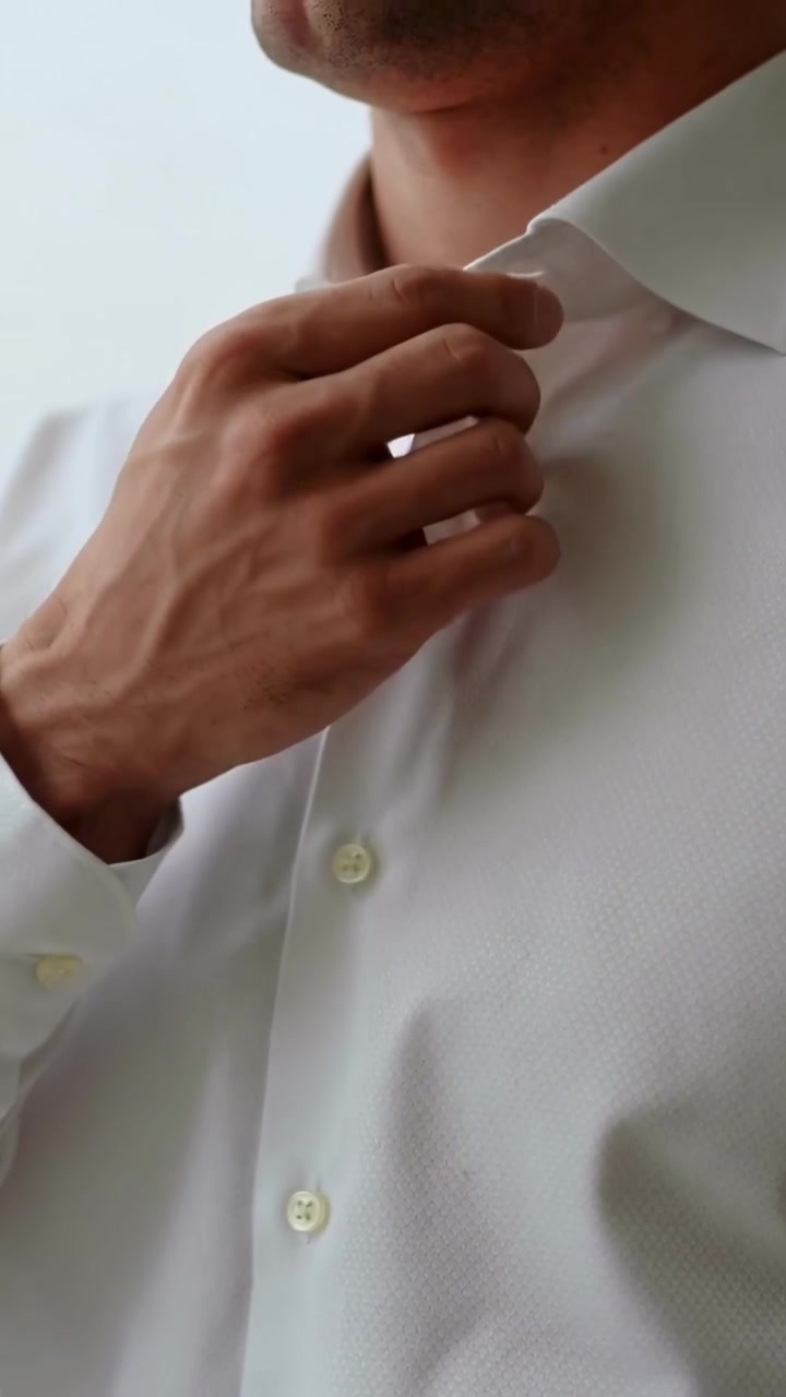 Video verticale: Uomo che si sistema, aggiustando il colletto e i bottoni della camicia bianca vicino alla finestra, preparandosi per una riunione
