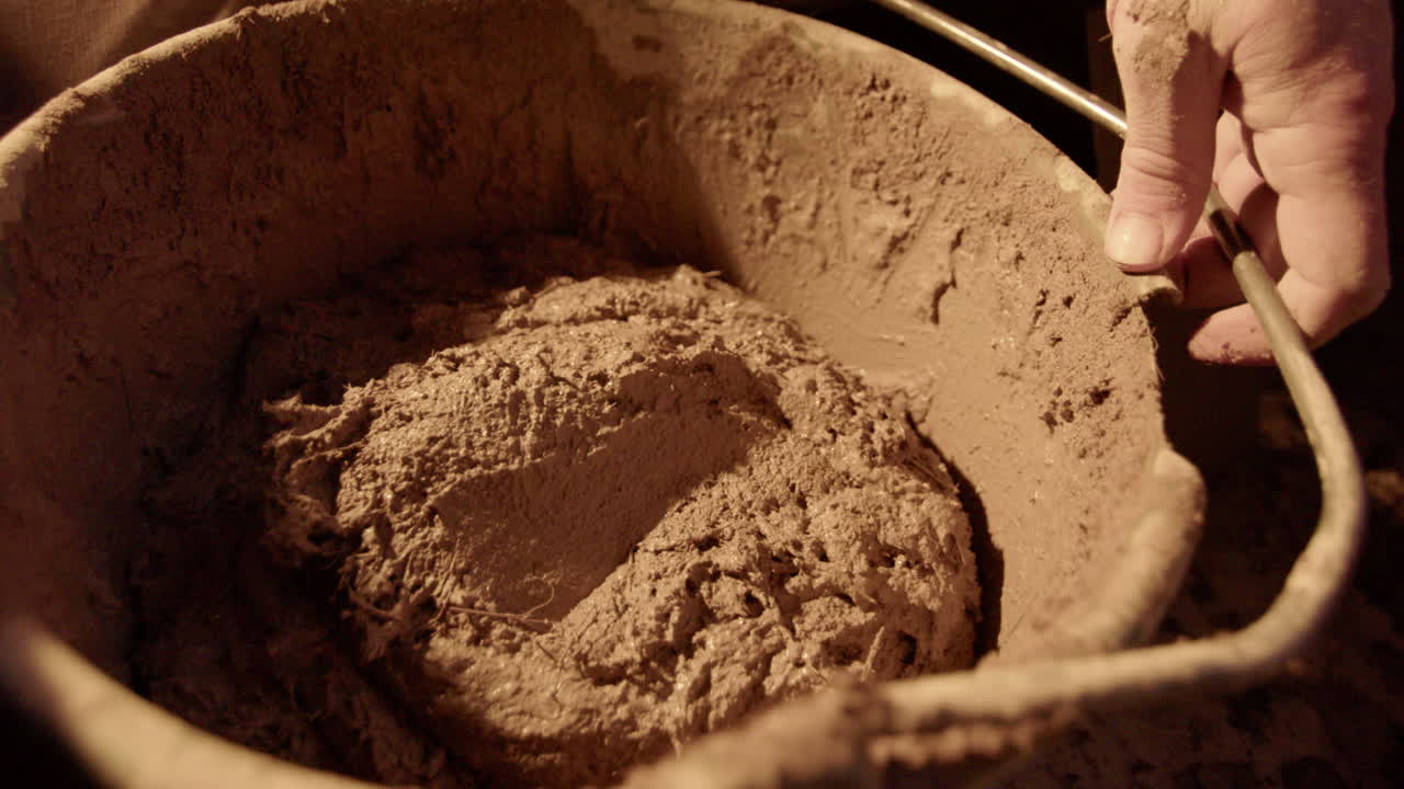 acercar, cámara lenta: la mezcla de arcilla se vierte en el balde de los yeseros