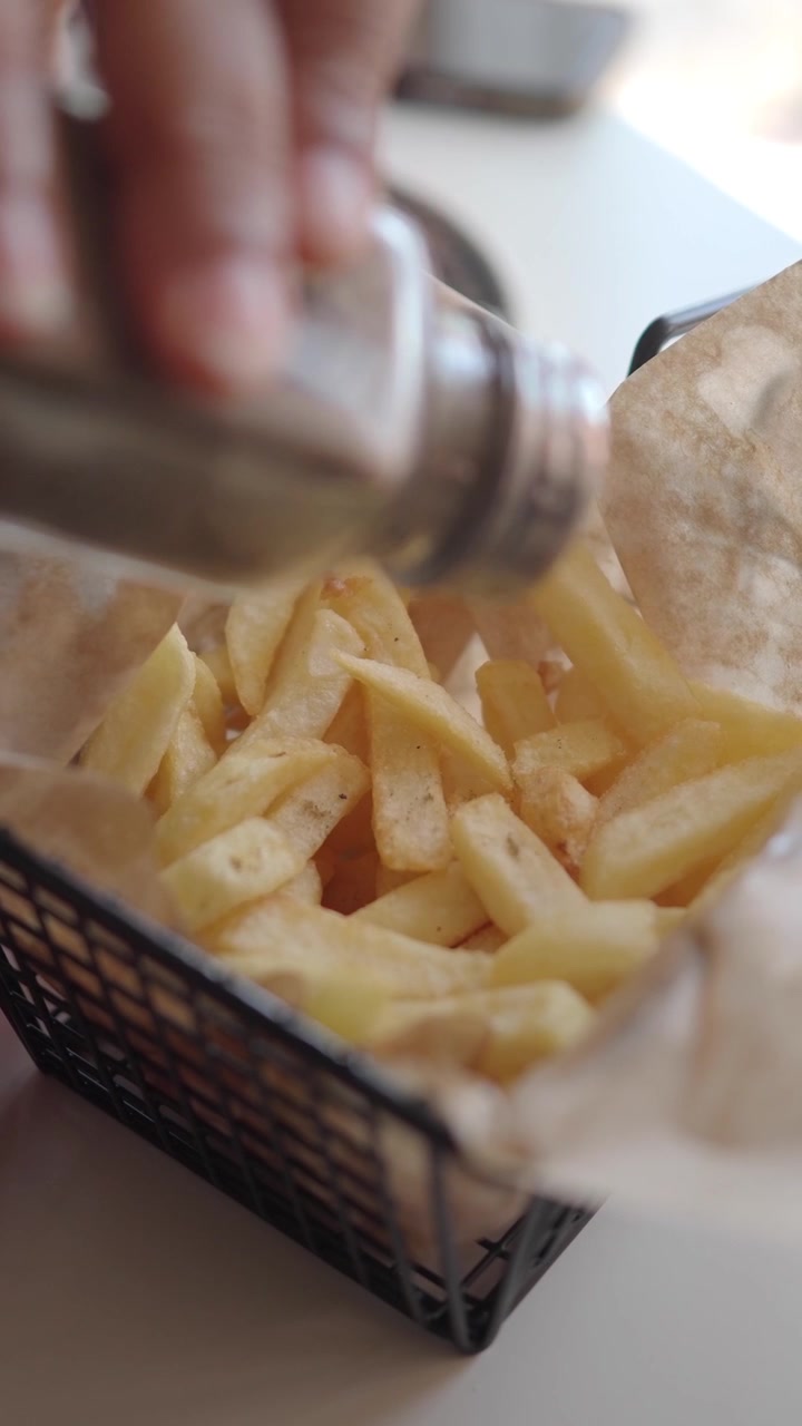 Seasoning Fresh French Fries in a Metal Basket
