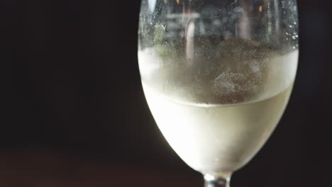 a glass of chilled white wine is gently swirled, creating visible motion and condensation. soft, moody lighting highlights the liquid’s clarity and coolness
