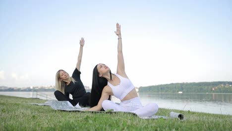 two european young women are doing yoga while sitting on the shore of the lake two european young women are doing yoga while sitting on the shore of the lake against the background of the sky yoga poses yoga in the fresh air on the shore of a morning calm lake health concept