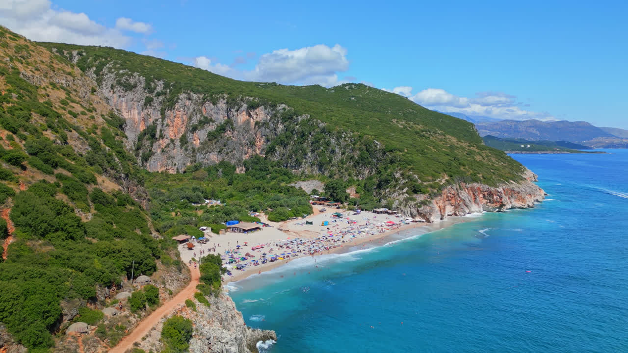 Aerial drone backward moving shot over tourists thronging on secluded Gjipe Beach in Dhermi, Albania on a sunny day